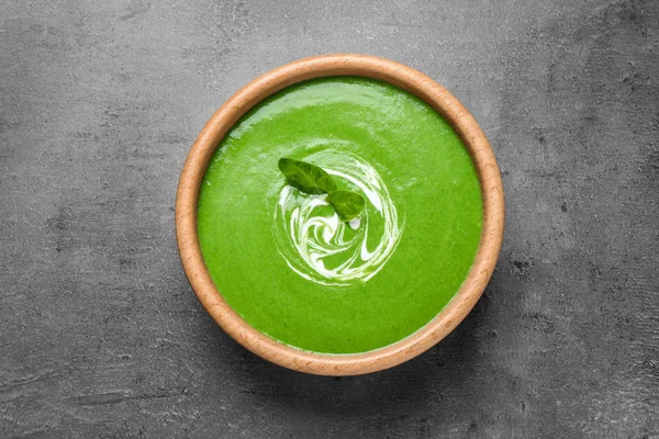 Bowl of healthy green soup with fresh spinach on grey table, top view