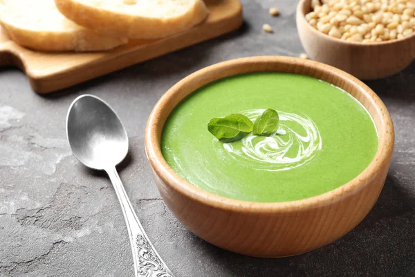 Bowl of healthy green soup with fresh spinach on grey table