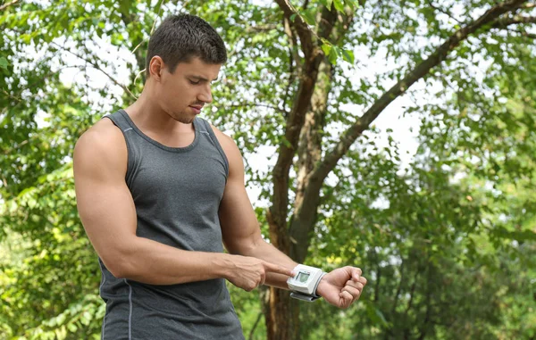 Hombre joven comprobando el pulso con dispositivo médico después del entrenamiento al aire libre — Foto de Stock
