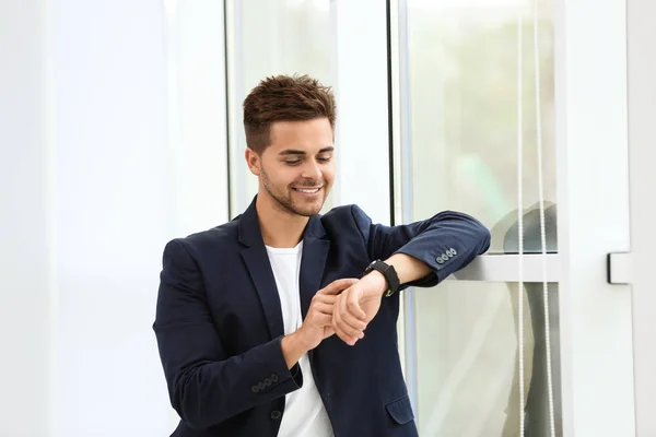 Portret van knappe jonge man kijken naar horloge in de buurt van venster — Stockfoto