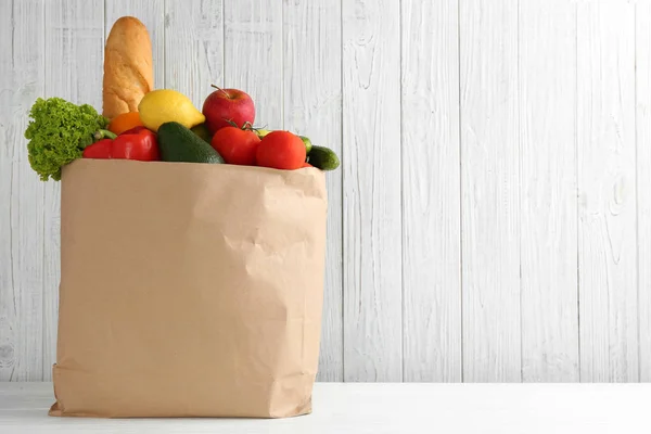 Nákupní taška s různými potravinami na stole s bílým dřevěným pozadím. Místo pro text — Stock fotografie
