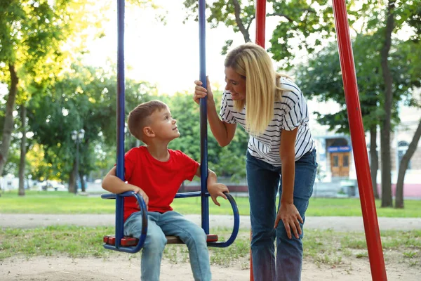 Bambinaia e carino bambino su swing in parco — Foto Stock