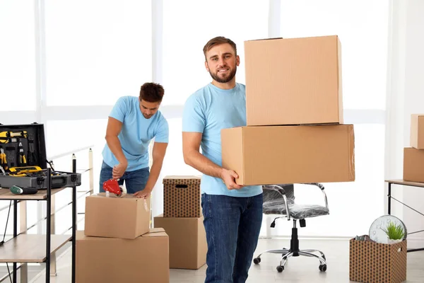 Trabajador joven con cajas de cartón y su colega en la oficina. Servicio móvil — Foto de Stock