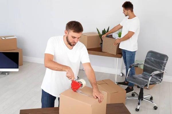 Young worker packing box and his colleague in office. Moving service