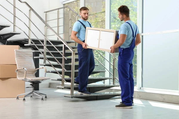 Профессиональные рабочие несут шкаф на лестнице в офисе. Услуги по перевозке — стоковое фото