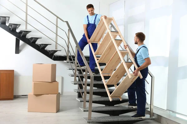 Профессиональные рабочие несут деревянные стойки на лестнице в офисе. Услуги по перевозке — стоковое фото