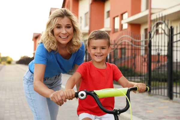 Счастливая мать учит своего сына кататься на велосипеде в городе — стоковое фото