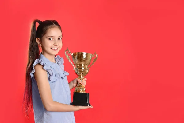 赤い背景に黄金の勝利カップを持つ幸せな女の子。テキスト用のスペース — ストック写真