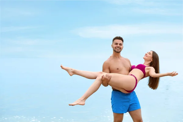 Jovem segurando sua namorada de biquíni na praia, espaço para texto. Casal encantador — Fotografia de Stock