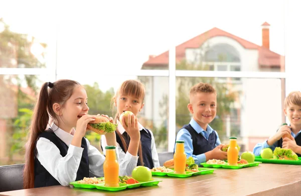 Niños felices en la mesa con comida saludable en el comedor escolar — Foto de Stock