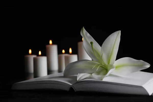 Weiße Lilie, Buch und verschwommene brennende Kerzen auf dem Tisch in der Dunkelheit, Nahaufnahme mit Platz für Text. Begräbnissymbol — Stockfoto