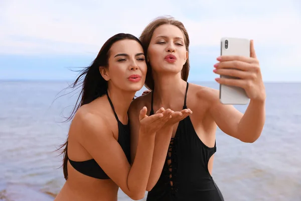 Mujer joven en bikini con novia tomando selfie en la playa. Hermosa pareja. — Foto de Stock