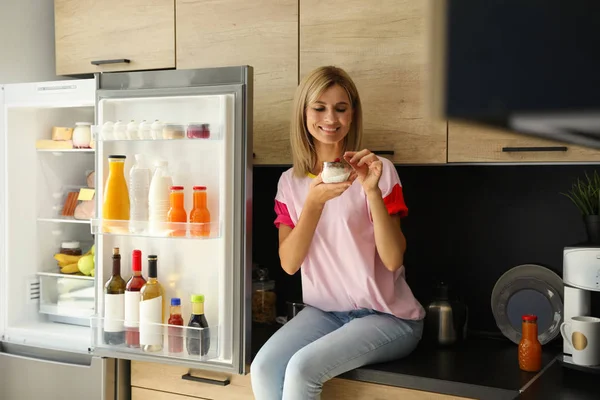 Frau isst Dessert neben Kühlschrank in Küche — Stockfoto