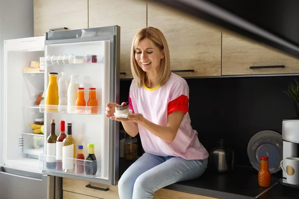 Žena s dezertem poblíž chladničky v kuchyni — Stock fotografie