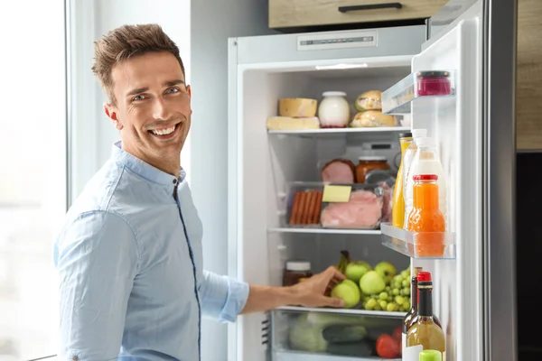 Hombre sacando manzana del refrigerador en la cocina — Foto de Stock