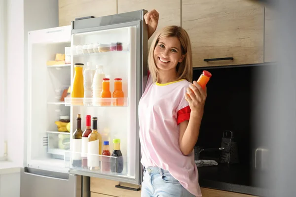 Žena s lahví šťávy blízko chladničky v kuchyni — Stock fotografie