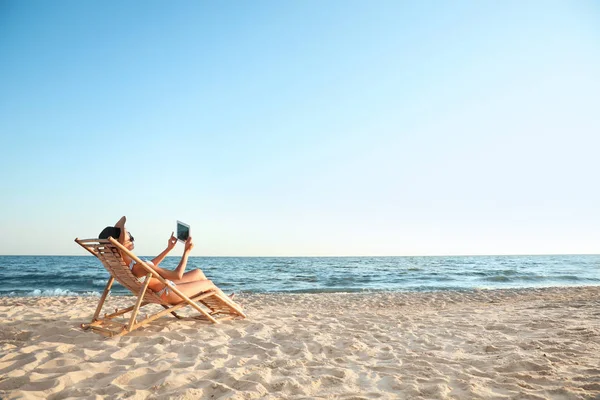 Jonge vrouw met Tablet ontspannen in terrasstoel op het strand — Stockfoto