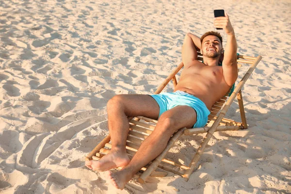 Joven tomando selfie en tumbona en la playa — Foto de Stock