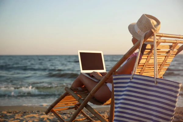 Mujer joven con portátil en la silla de cubierta en la playa — Foto de Stock