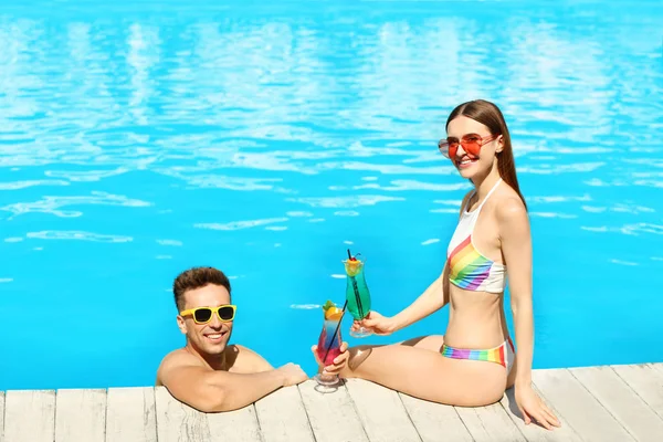 Šťastný mladý pár s koktejly odpočívajícím v bazénu — Stock fotografie