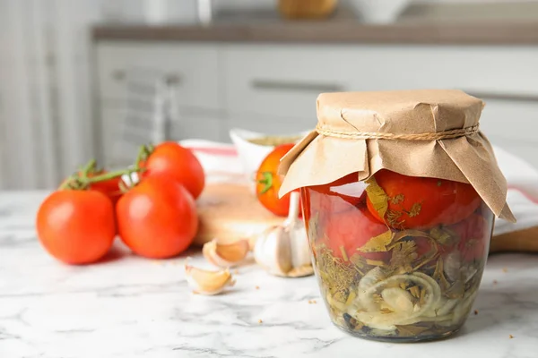 Tomates en vinagre en frasco de vidrio y productos en mesa de mármol blanco en la cocina — Foto de Stock