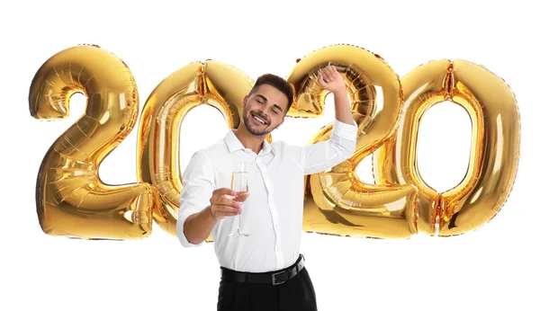Happy young man with glass of champagne near golden 2020 balloons on white background. New Year celebration — Stock Photo, Image