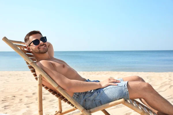 Hombre joven relajándose en la silla de cubierta en la playa de arena — Foto de Stock