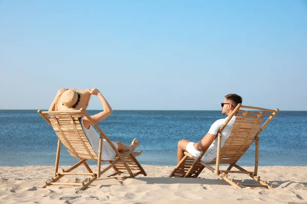 Pareja joven relajándose en tumbonas en la playa —  Fotos de Stock