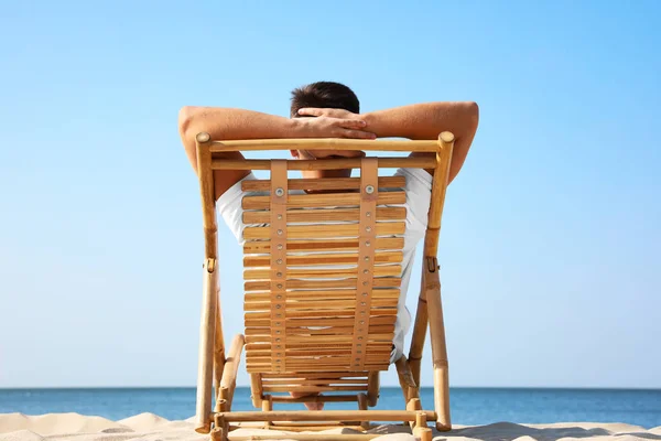 Νέος άνθρωπος χαλαρωτικό στο κατάστρωμα καρέκλα στην αμμώδη παραλία — Φωτογραφία Αρχείου