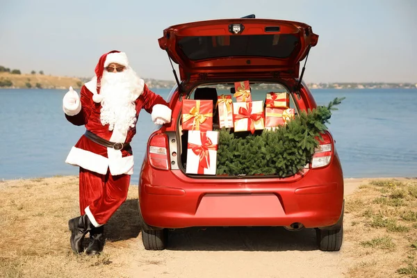 Authentic Santa Claus near car with open trunk full of presents and fir tree outdoors — Stock Photo, Image