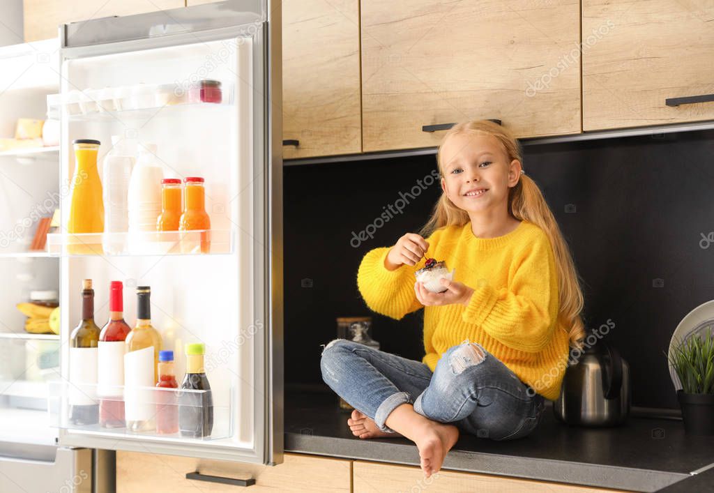 Girl eating dessert near refrigerator in kitchen