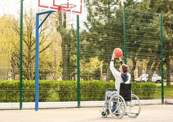 Młody człowiek na wózku inwalidzkim gra w koszykówkę na ziemi sportowej — Zdjęcie stockowe