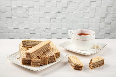 Beyaz ahşap masada çay fincan ile lezzetli gofret Tabak
