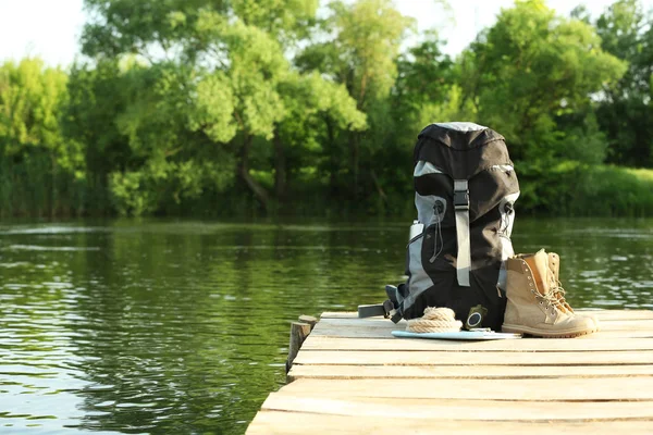 Sac à dos et matériel de camping sur jetée en bois près de la rivière. Espace pour le texte — Photo