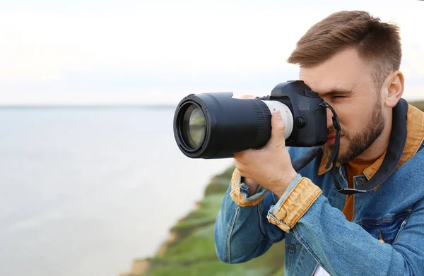 Mężczyzna fotografa biorąc obraz pięknej scenerii z profesjonalnym aparatem na zielonym wzgórzu. Miejsce na tekst — Zdjęcie stockowe