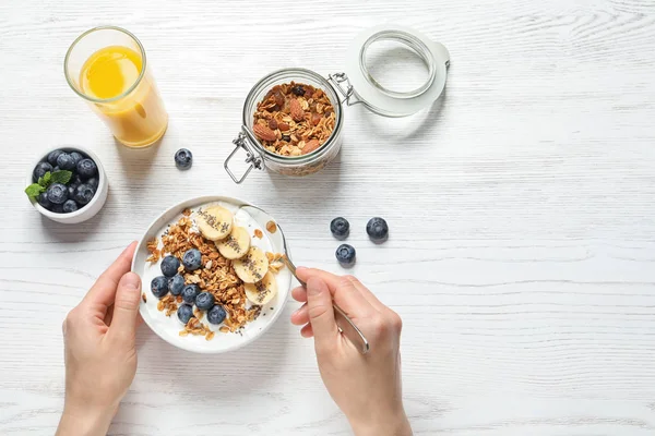 Mujer comiendo sabroso yogur con avena, plátano y arándanos en la mesa de madera blanca, vista superior. Espacio para texto — Foto de Stock