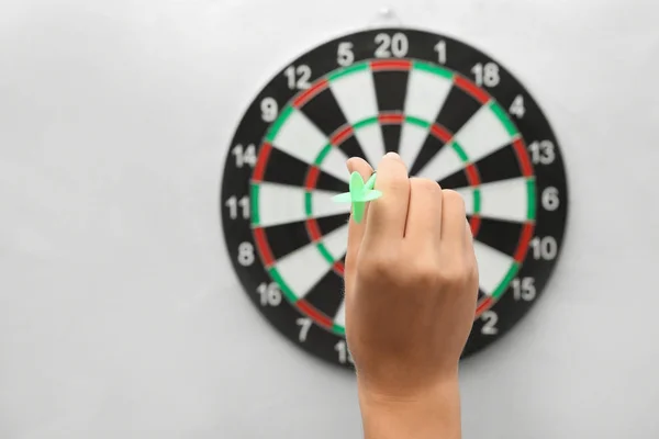 Vrouw gooien groene pijl bij dartbord op licht blauwe achtergrond, close-up. Ruimte voor tekst — Stockfoto