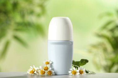 Bulanık arka plan karşı beyaz ahşap masa üzerinde Deodorant konteyner ve papatya