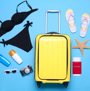 Mavi arka plan üzerinde sarı bavul ve plaj nesneleri, düz yatıyordu