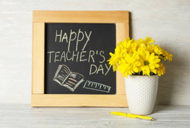 Yazıt Mutlu Öğretmenler Günü ve Hafif duvara karşı ahşap masa üzerinde çiçek vazo ile Chalkboard