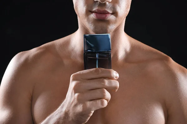 Young man with bottle of perfume on black background, closeup — Stock Photo, Image