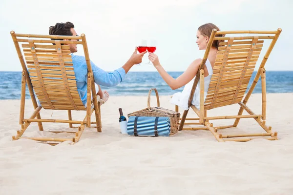 Glückliches junges Paar mit Weingläsern auf Liegestühlen am Meeresstrand — Stockfoto