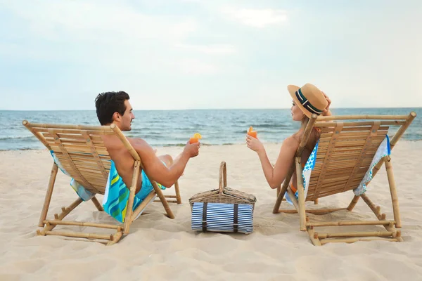 Feliz pareja joven con cócteles sentados en tumbonas en la playa de mar — Foto de Stock