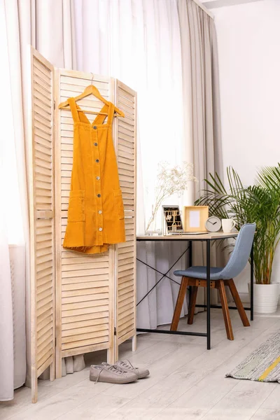 Yellow dress on wooden folding screen indoors. Interior design