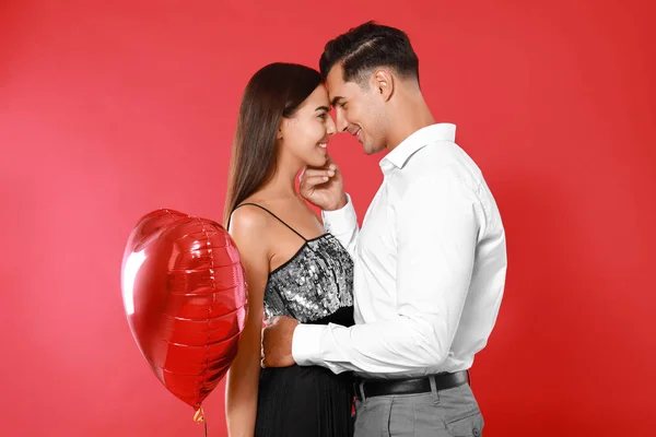 Casal bonito com balão em forma de coração no fundo vermelho — Fotografia de Stock