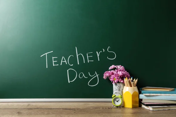 Green chalkboard with inscription TEACHER\'S DAY and vase of flowers on wooden table
