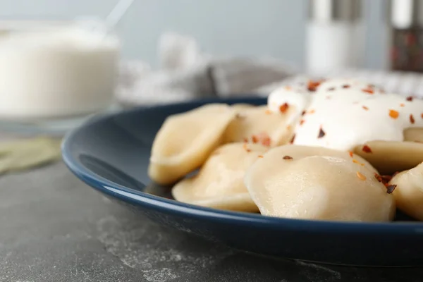 Delicious cooked dumplings with sour cream on grey table, closeup — Stock Photo, Image