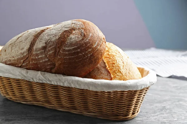 Laibe leckeres frisches Brot im Weidenkorb auf grauem Tisch, Nahaufnahme — Stockfoto