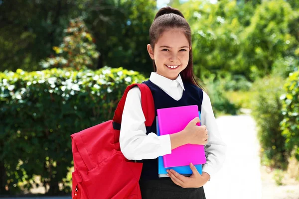 Schattig klein meisje in school uniform met rugzak en briefpapier op straat — Stockfoto