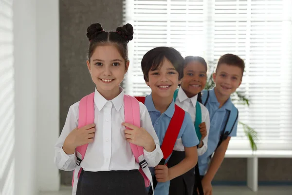 Crianças felizes em uniforme escolar com mochilas dentro de casa — Fotografia de Stock